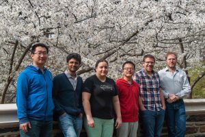 5 people pose in front of a blooming tree